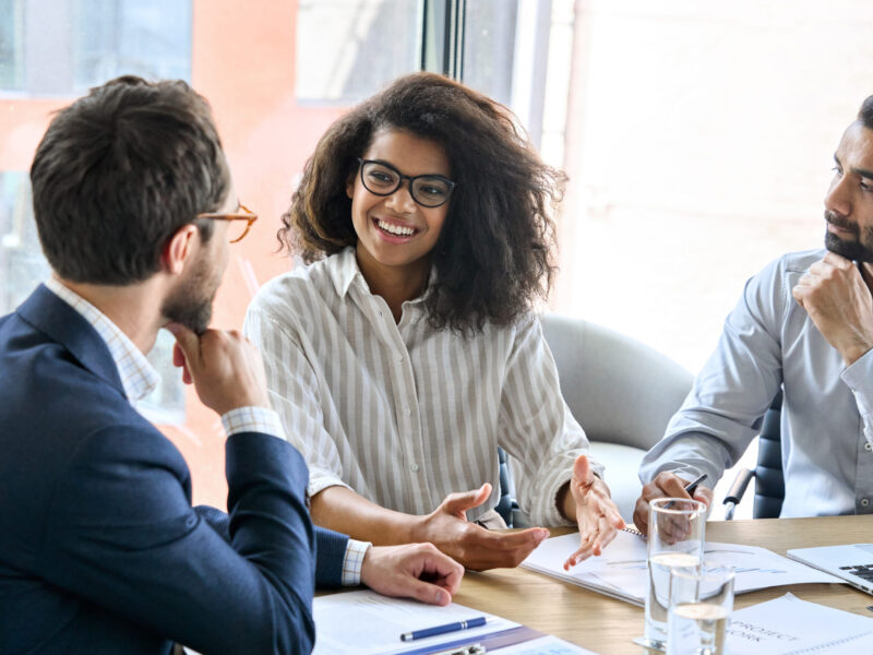 Two businessmen and a business woman sit around a table having a discussion.