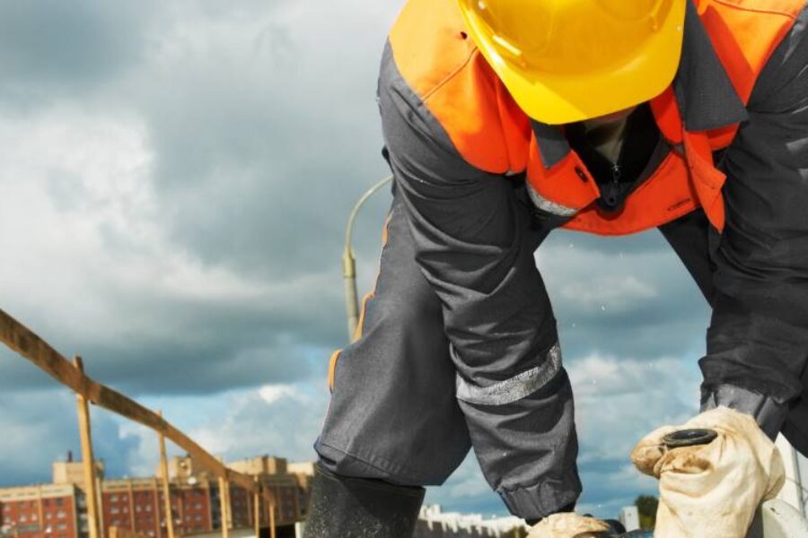 A construction worker is crouching down on top of a building site using a saw.