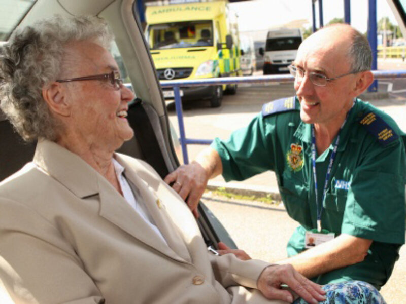 A paramedic is helping an elderly woman into a car.